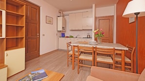 A compact kitchen with wooden cabinets, a dining table with chairs, a sofa, and a lamp.