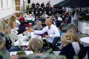 Un gruppo di persone sedute a tavoli all'aperto, impegnate in conversazioni e a mangiare.