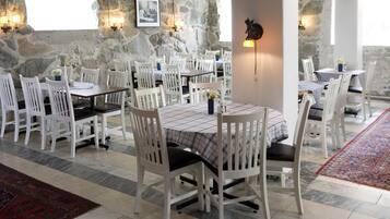 Un restaurante con sillas y mesas blancas, paredes de piedra y alfombra roja.