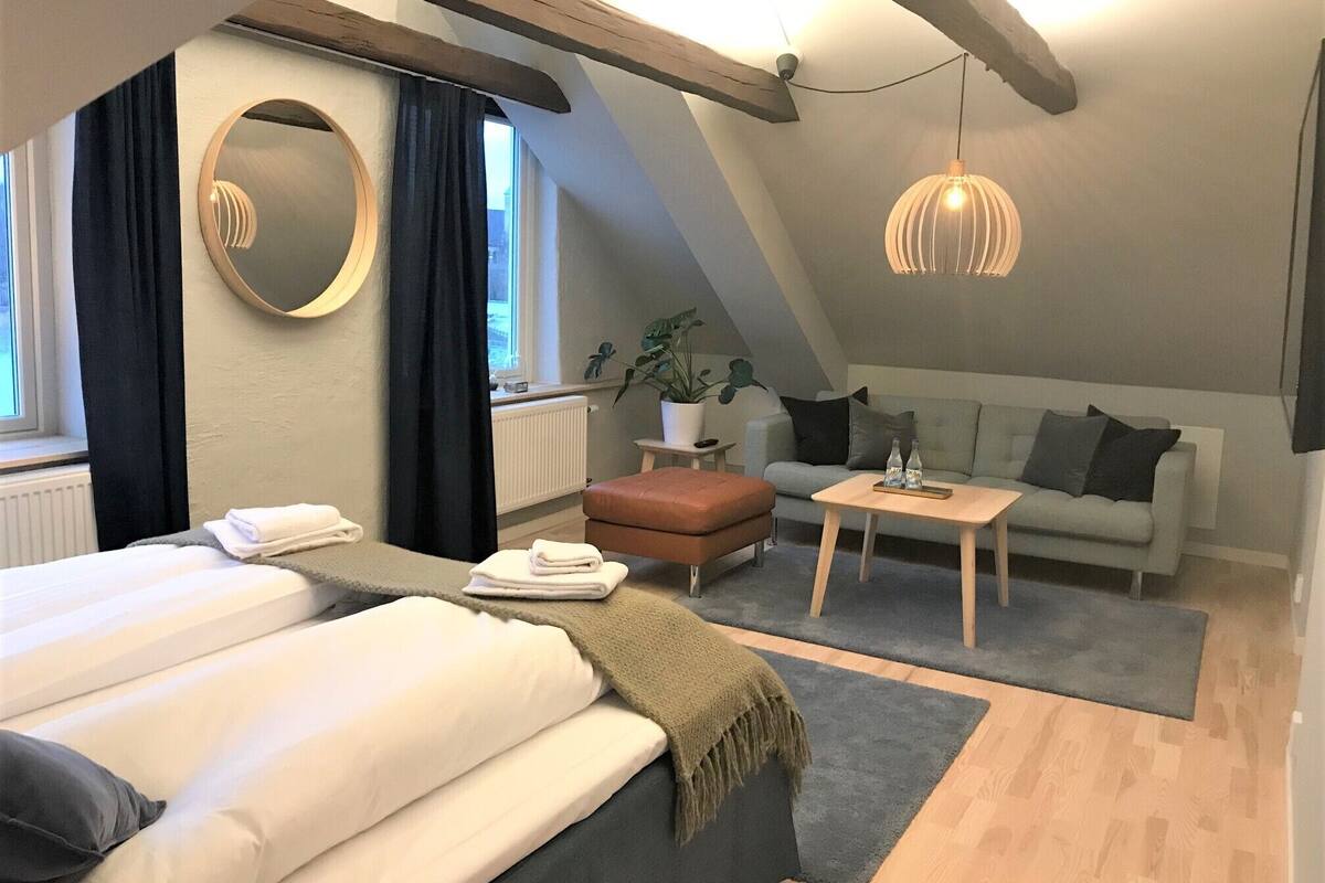A modern, well-lit room with a bed, a sofa, a small table, and a hanging light fixture.