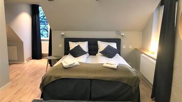 Une chambre à coucher moderne avec un grand lit, une petite table de chevet et une vue sur l’extérieur par une fenêtre.