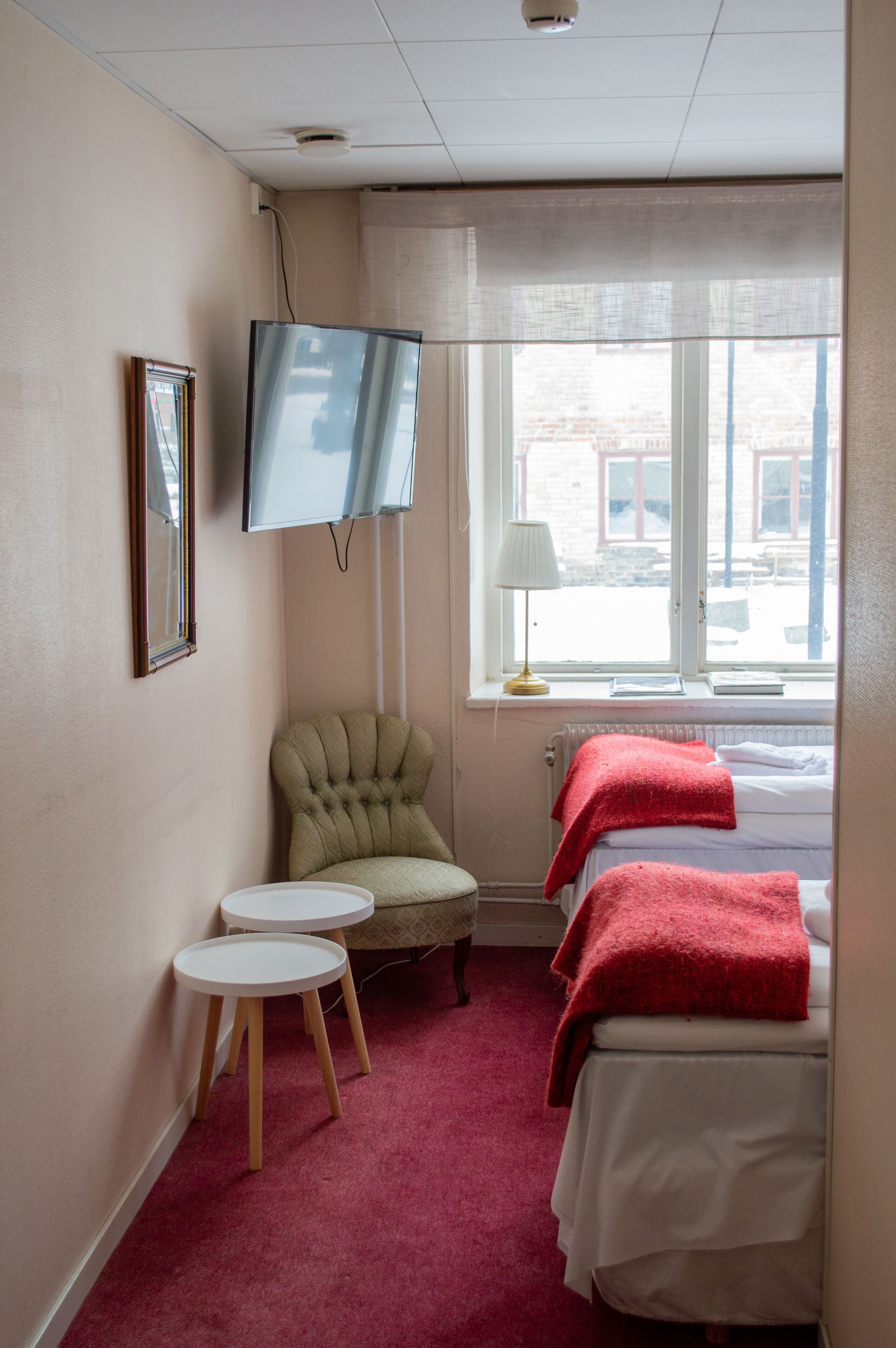 A hotel room with a bed, a television, a chair, two small tables, and a window with a view of the street.