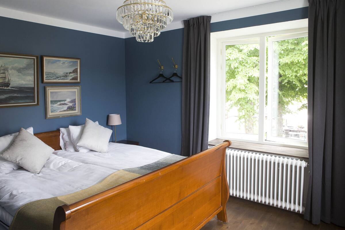 A bedroom with a wooden bed, white bedding, a chandelier, and a window with curtains.