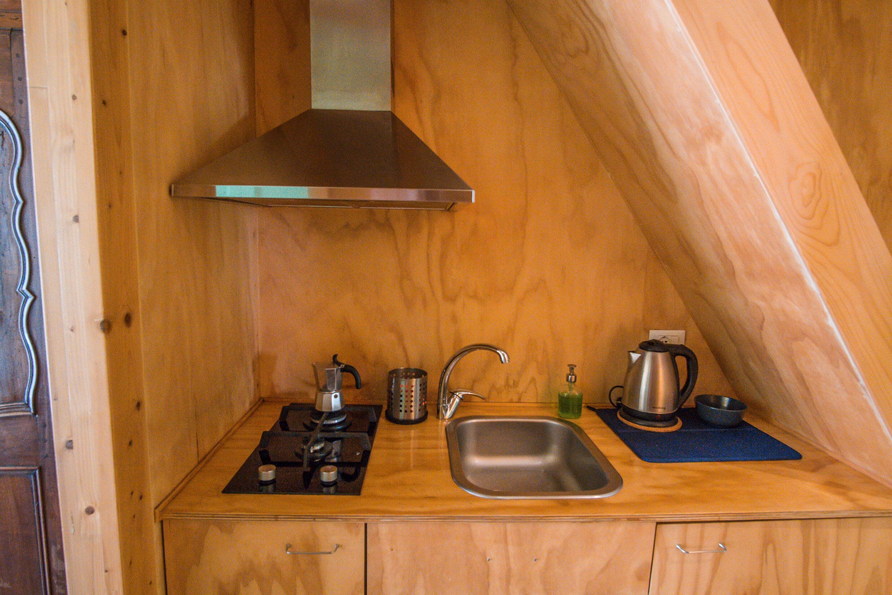 Una cocina compacta con un lavamanos de acero inoxidable, una estufa a gas y una campana extractora.