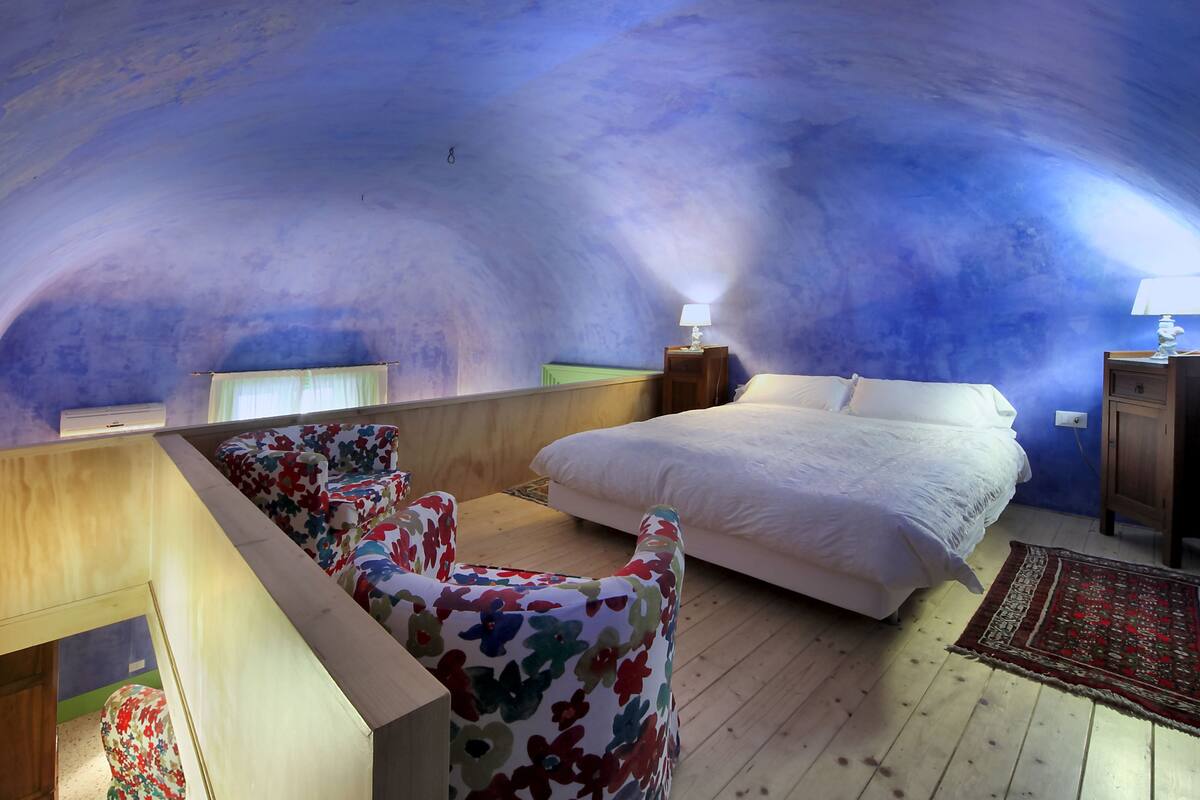 Une chambre à coucher avec un lit, une table de chevet, une lampe, une chaise et un plancher en bois.