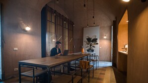 Una habitación amplia con una mesa larga, sillas y una persona trabajando en un ordenador portátil.