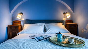 Una cama bien hecha con sábanas blancas, dos lámparas de noche, una bandeja con cafetera, taza y cuchara, y una revista sobre la cama.