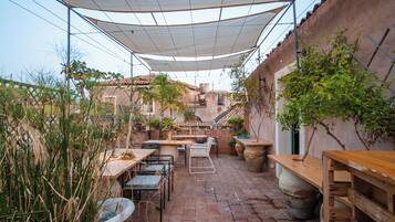 Una terrazza con tavolo e sedie, circondata da piante in vaso e una zona ombreggiata.