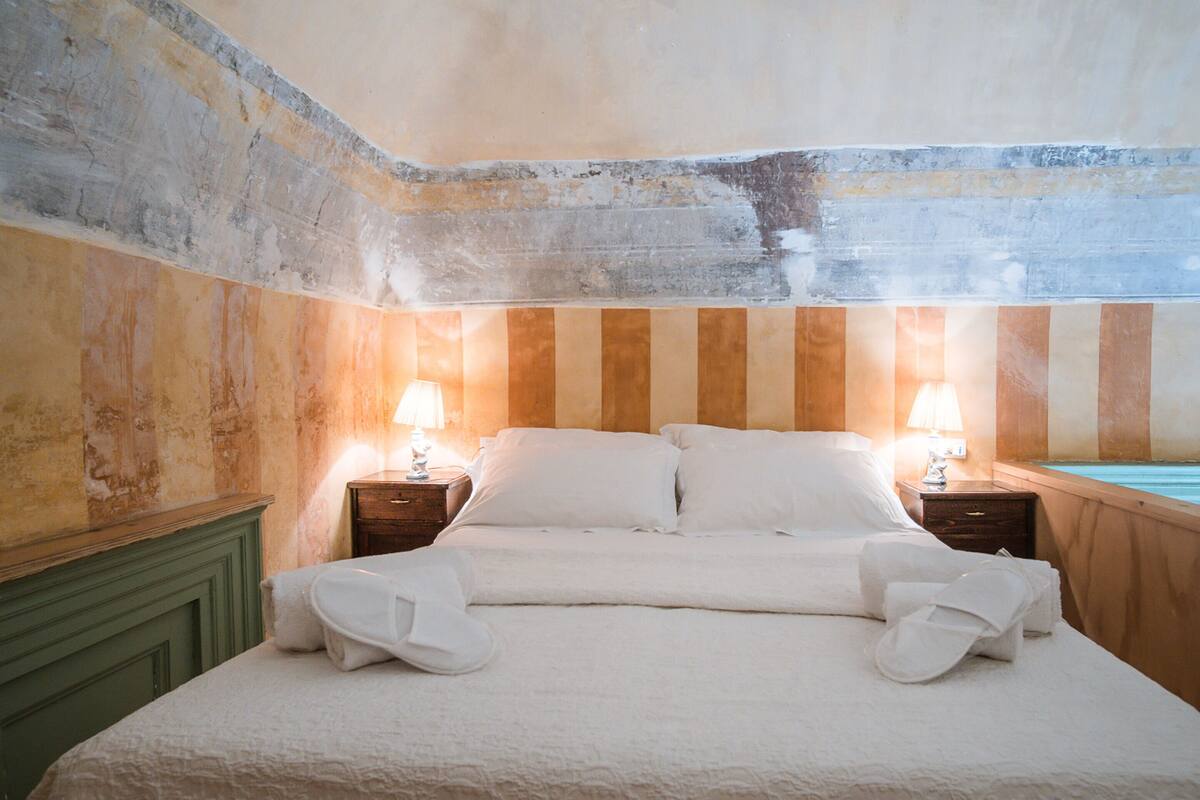 Une chambre d’hôtel avec un lit, deux tables de chevet avec des lampes, une tête de lit en bois et une vue sur une piscine.