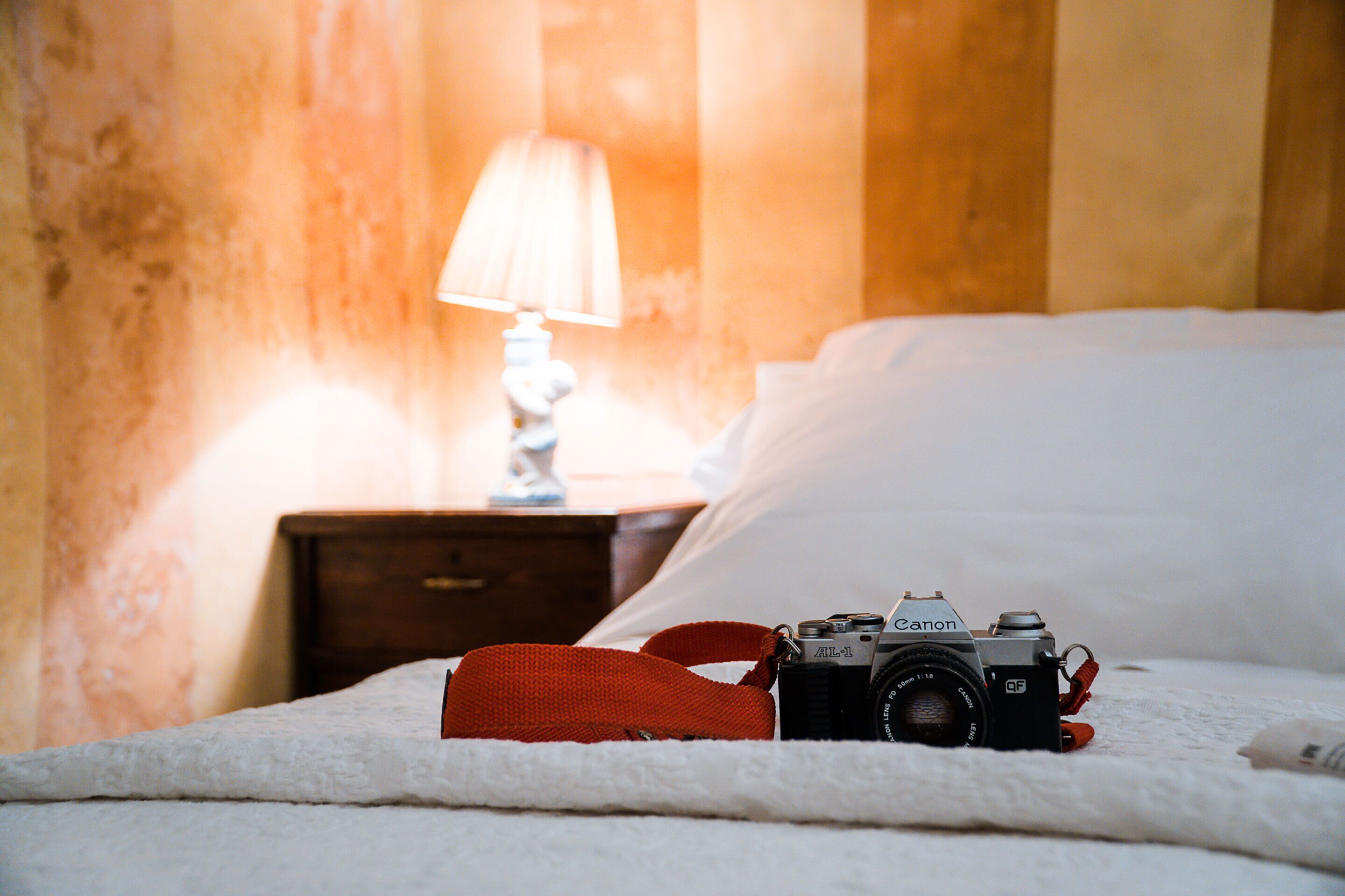 A bed with a Canon camera and a red strap on it.