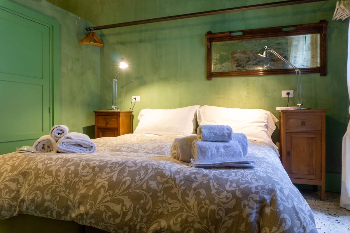 Un lit bien fait, recouvert d’une couvre-lit à motifs, deux tables de chevet avec des lampes et une petite table en bois placée près du lit.