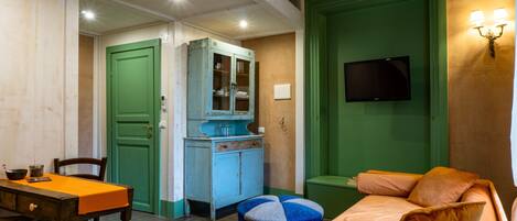Une pièce avec une porte verte, un téléviseur fixé au mur, une table en bois recouverte d’une nappe orange et un lit avec une literie orange.