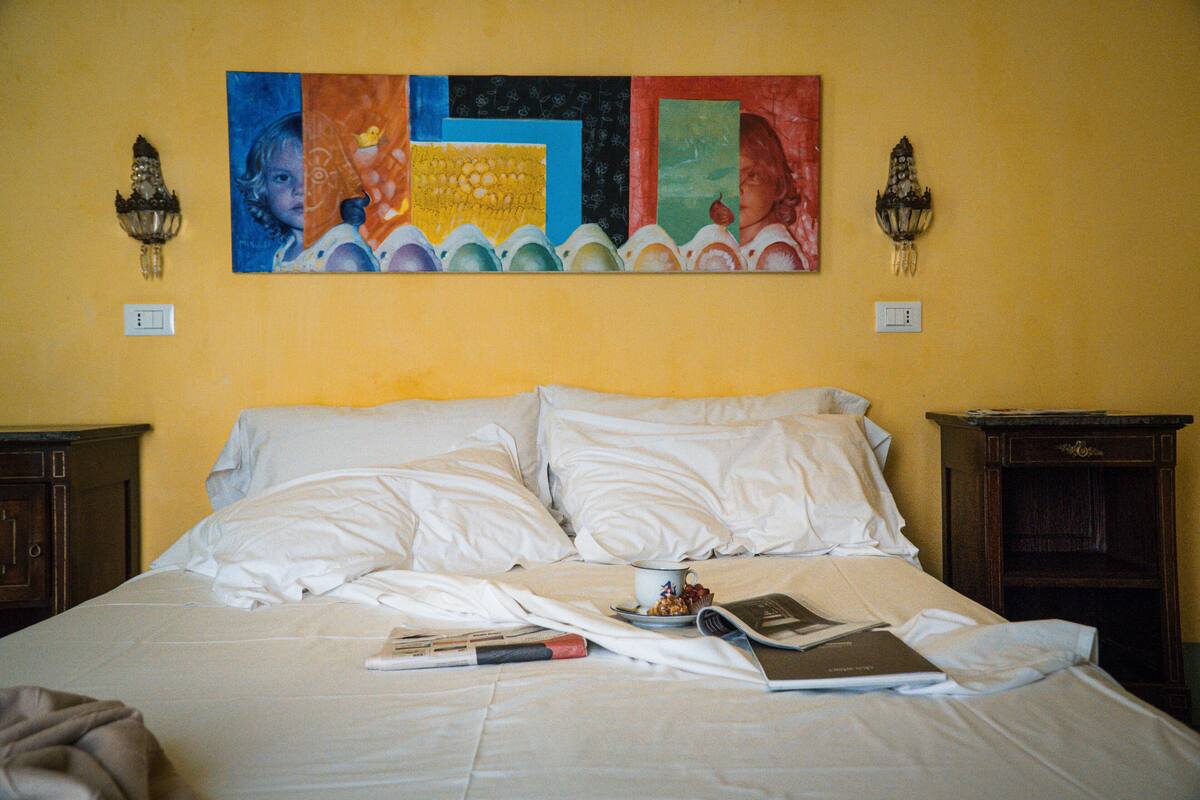 Un lit avec du linge de lit blanc, un tableau au-dessus et deux appliques murales.