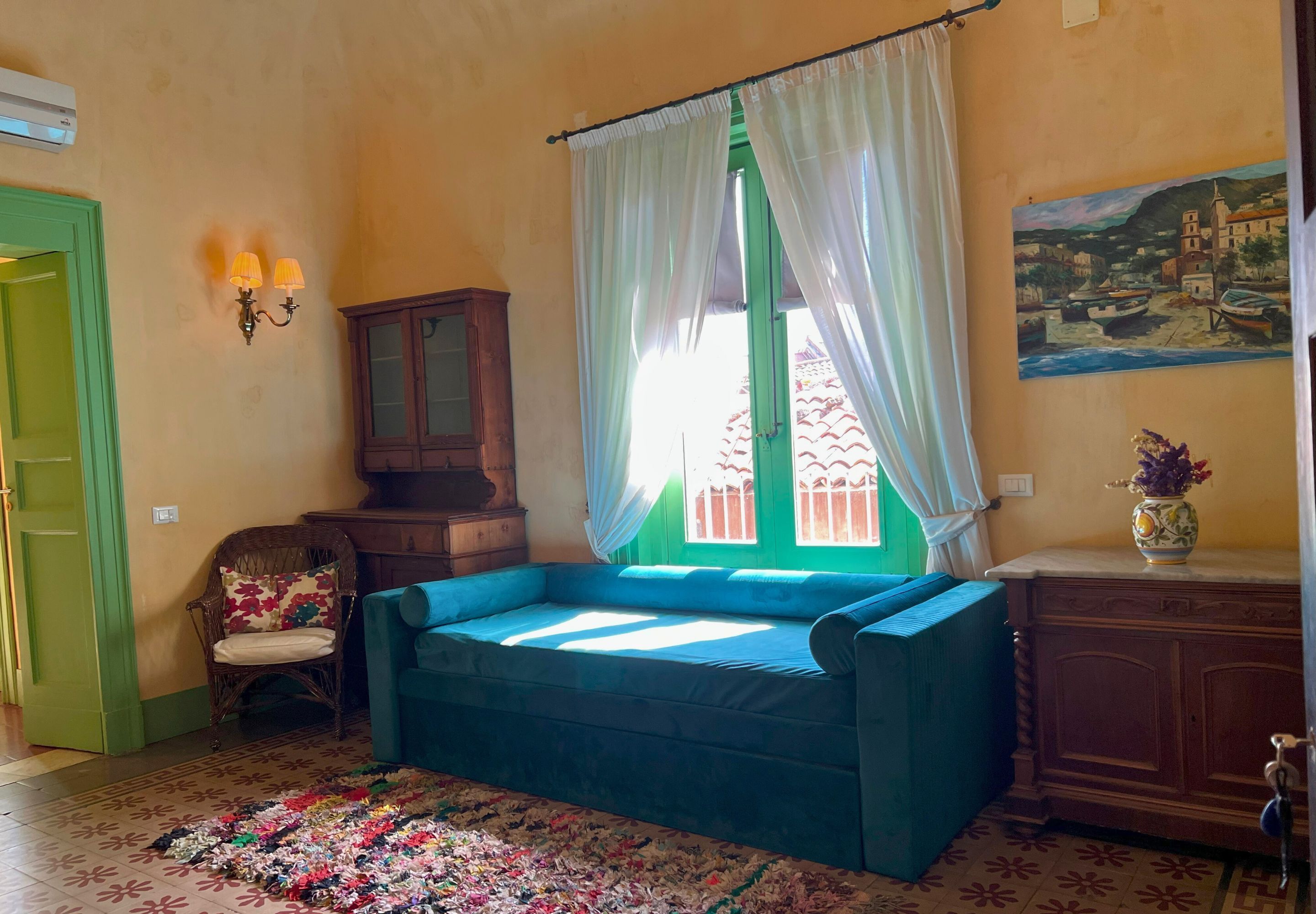 Una habitación con un sofá azul, una silla, un armario, un cuadro y una ventana con cortinas.