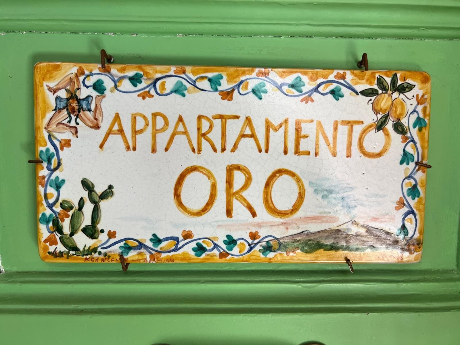 A sign with the text "APARTAMENTO ORO" surrounded by colorful floral and cactus designs.