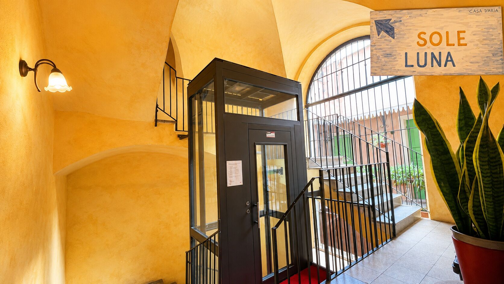 Una escalera con una puerta de cristal, una planta en maceta y un cartel que dice 'SOLE LUNA'.
