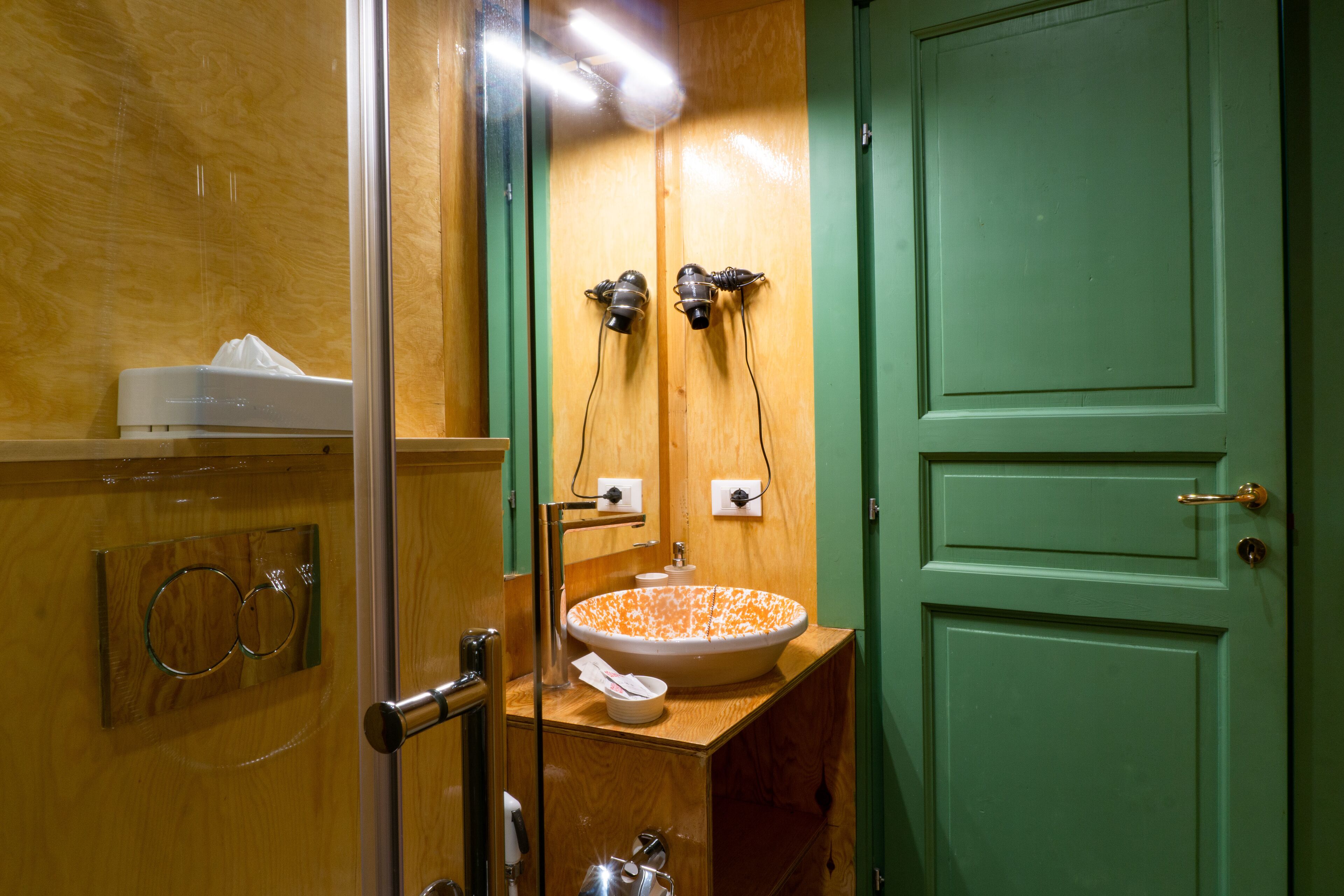 A bathroom with a wooden vanity, a sink with a patterned bowl, and a green door.