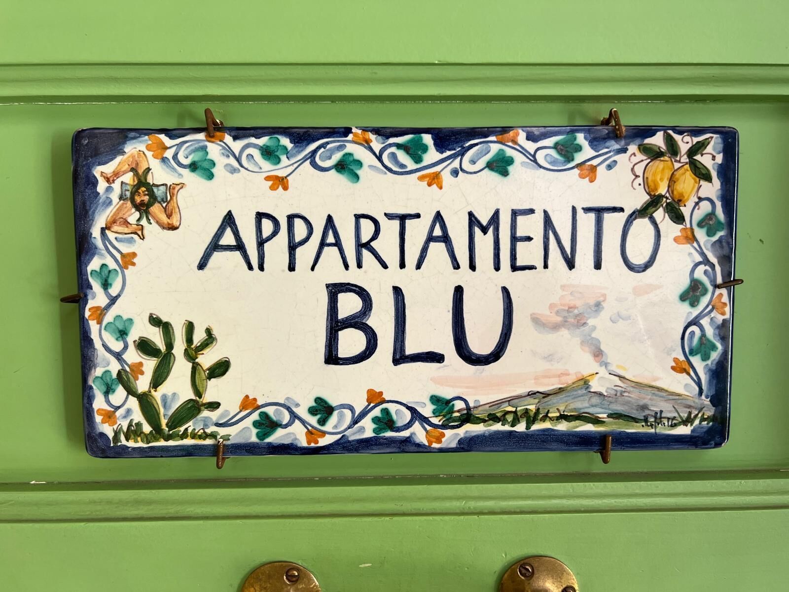 Et farverigt skilt til en lejlighed med teksten "APARTAMENTO BLU" samt dekorative elementer som blomster og en fugl.
