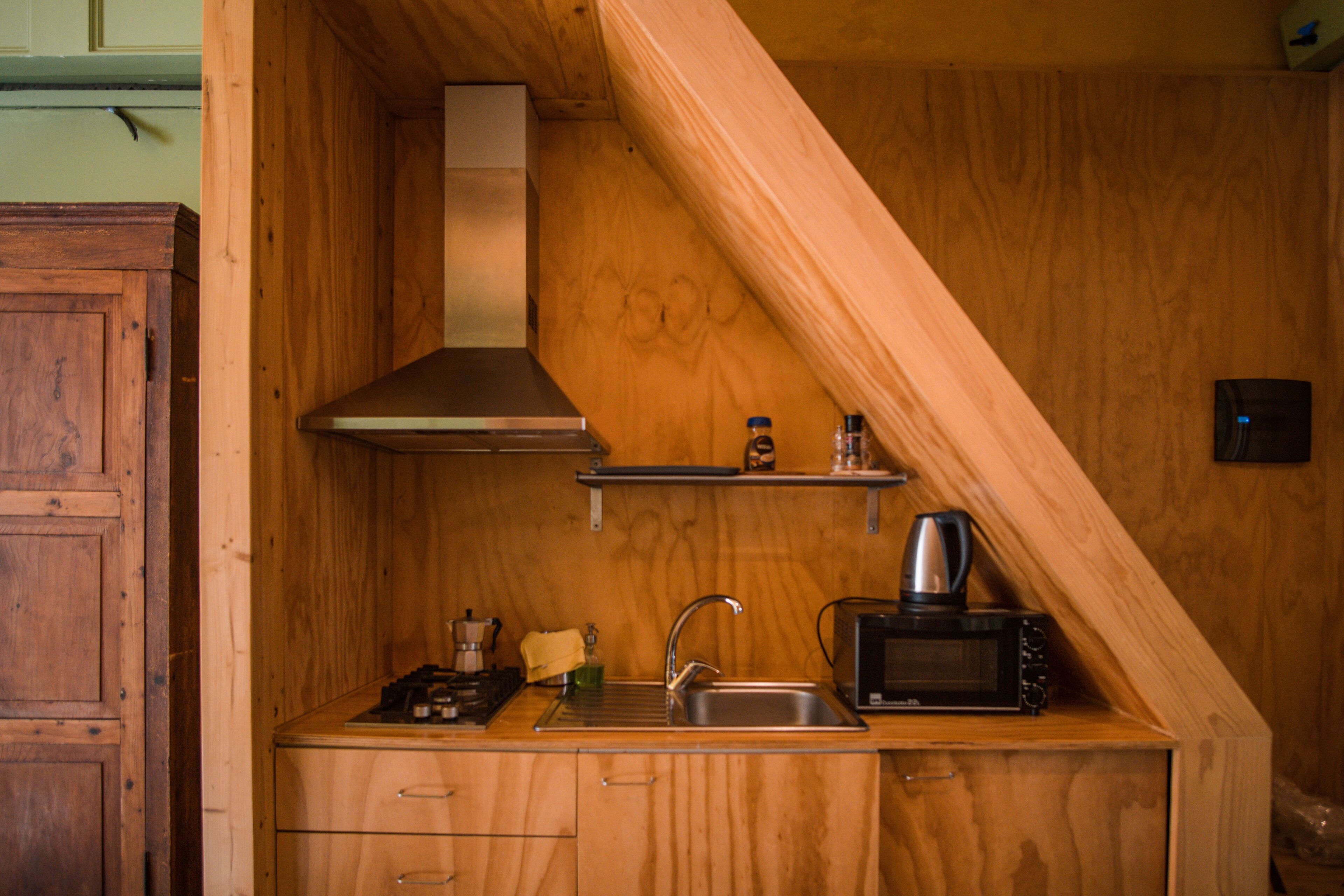 A compact kitchen with wooden cabinetry, a stainless steel sink, a microwave, and a coffee maker.