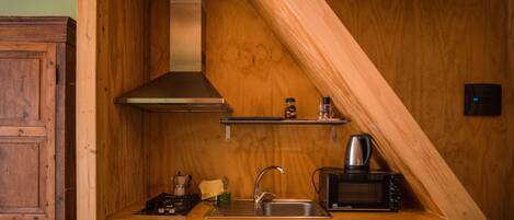 A compact kitchen with wooden cabinetry, a stainless steel sink, a microwave, and a coffee maker.