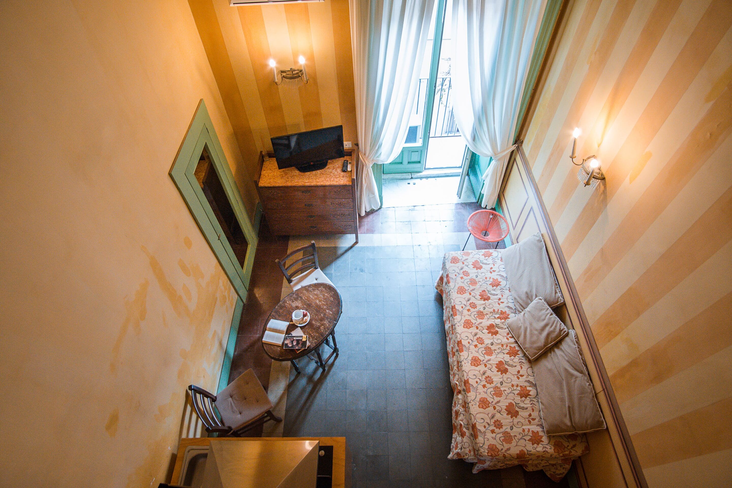 Un couloir étroit comprenant un lit, une table avec une chaise, une petite table avec une chaise et un téléviseur posé sur une commode.