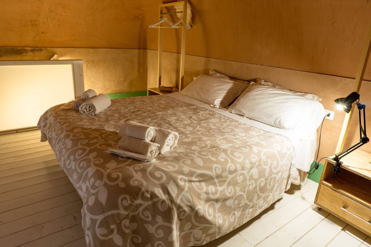 Un lit bien fait, avec une couvre-lit à motifs et des oreillers, une lampe de chevet et une table de chevet en bois avec une lampe.