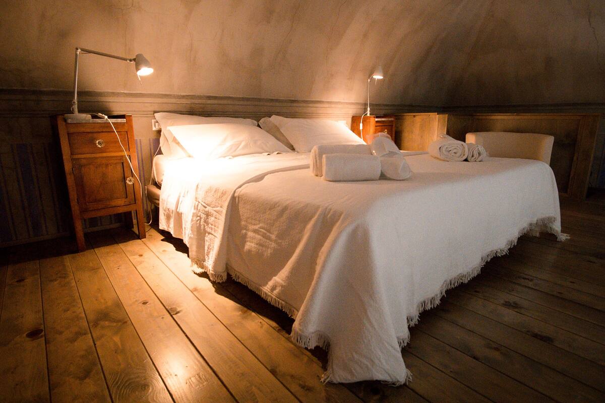 Une chambre confortable avec un plancher en bois, un lit recouvert de draps blancs, deux lampes de chevet et une table de chevet en bois.