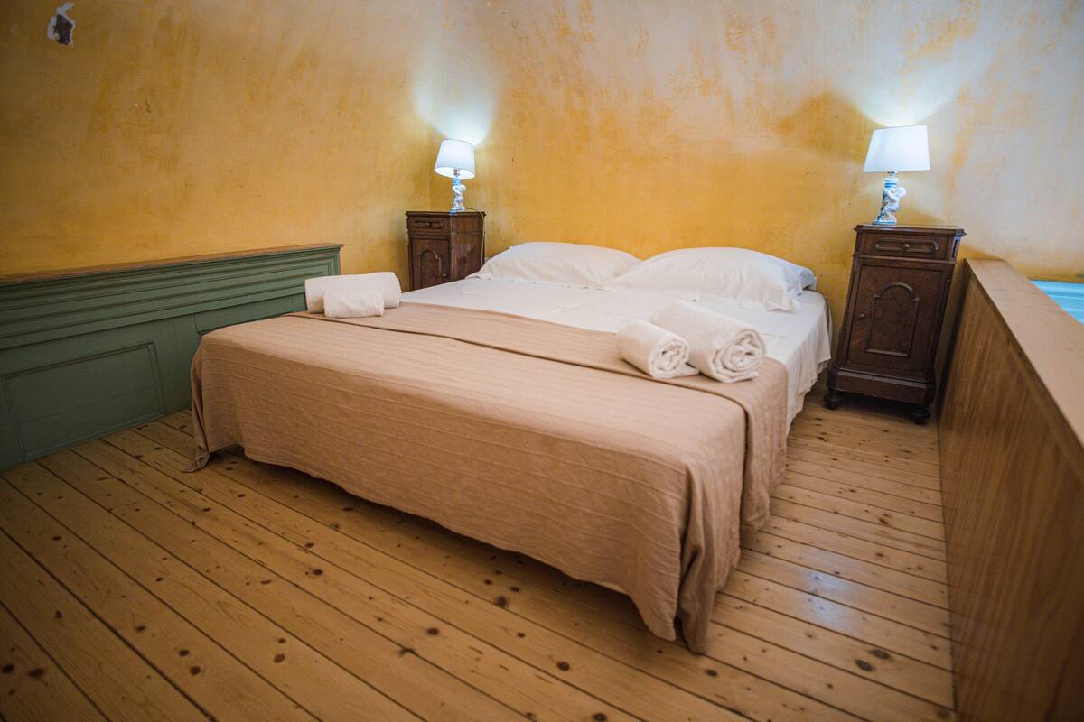 Un lit bien fait, avec une tête de lit verte, deux tables de chevet avec des lampes et un plancher en bois.