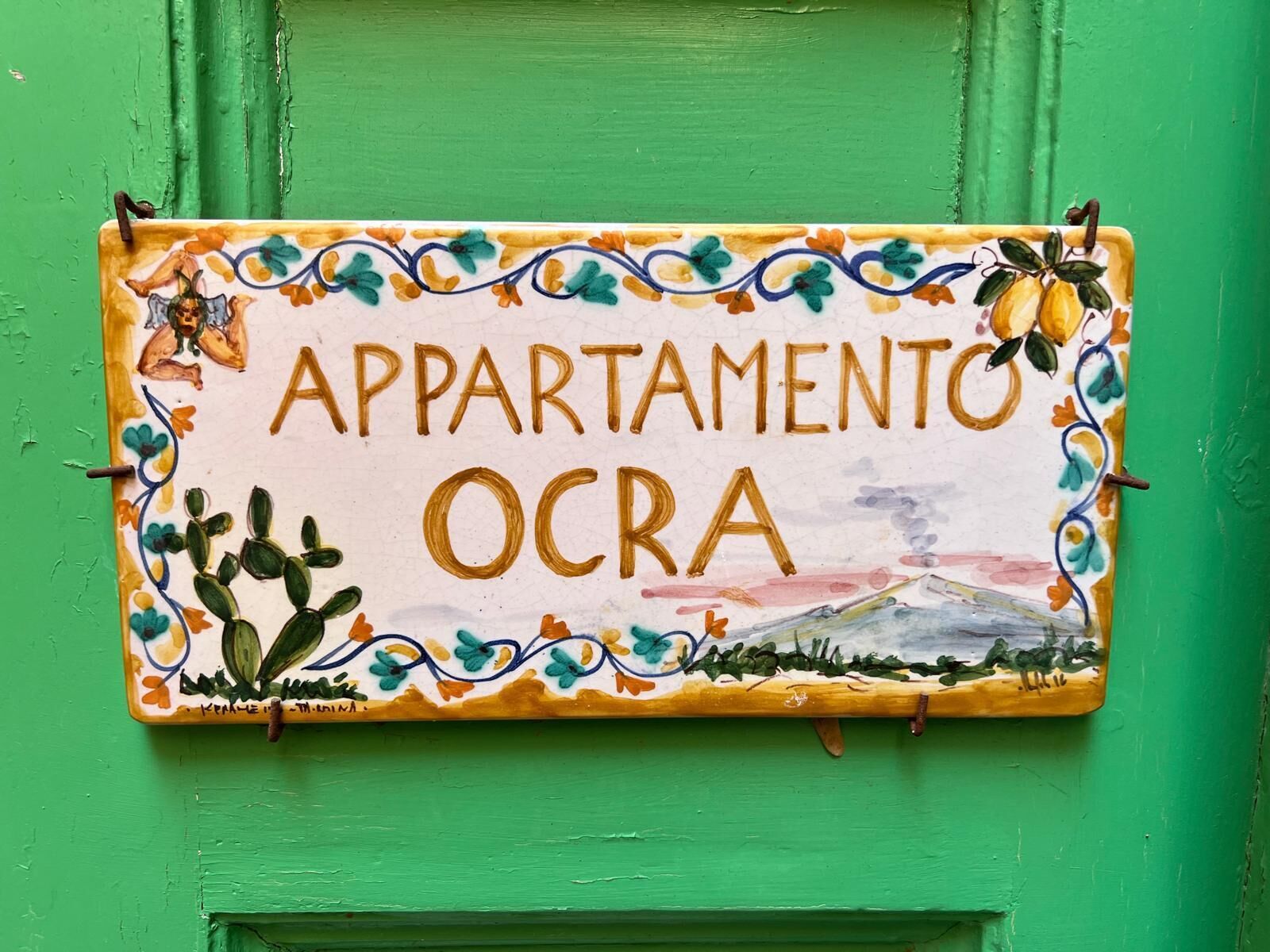 Ein Schild mit dem Schriftzug 'APARTAMENTO OCRA', umgeben von dekorativen Elementen.
