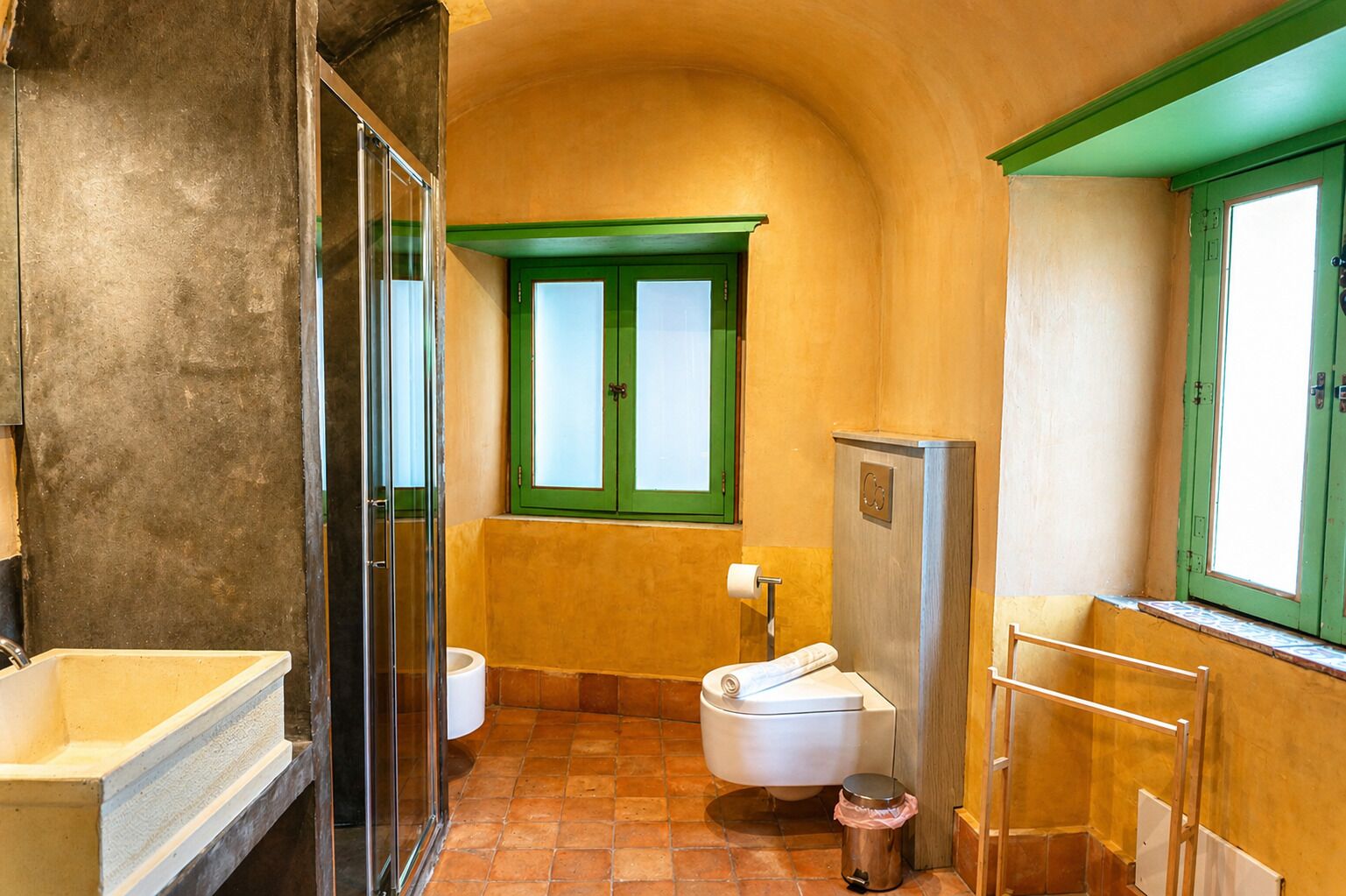 A bathroom with a shower, toilet, and sink, featuring green window frames and a tiled floor.