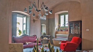 Una sala de estar acogedora con un sofá rojo, un sillón rojo y un sillón estampado. Hay una planta en primer plano y un aparador de madera al fondo.