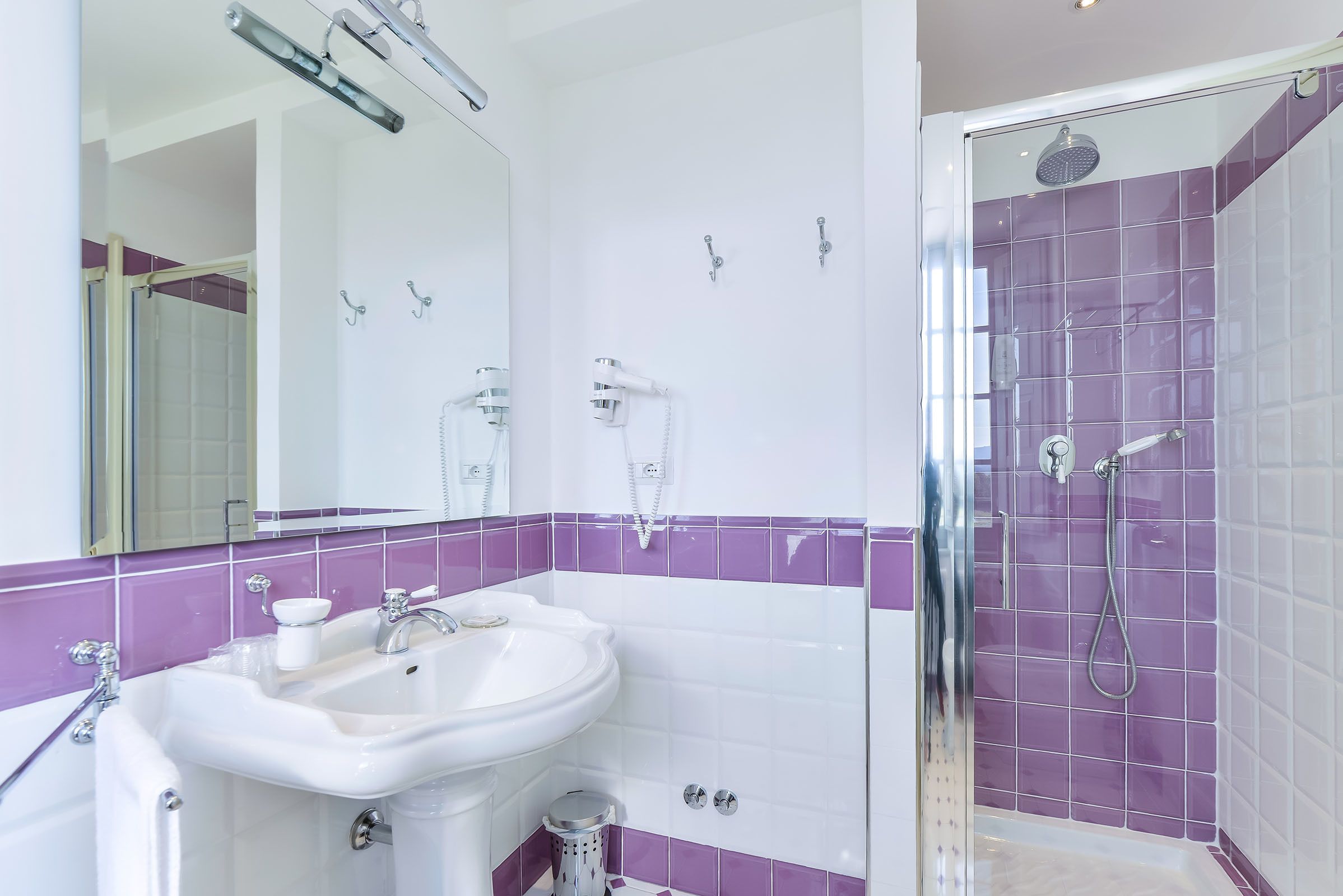 A bathroom with a white sink, mirror, and purple-tiled shower area.