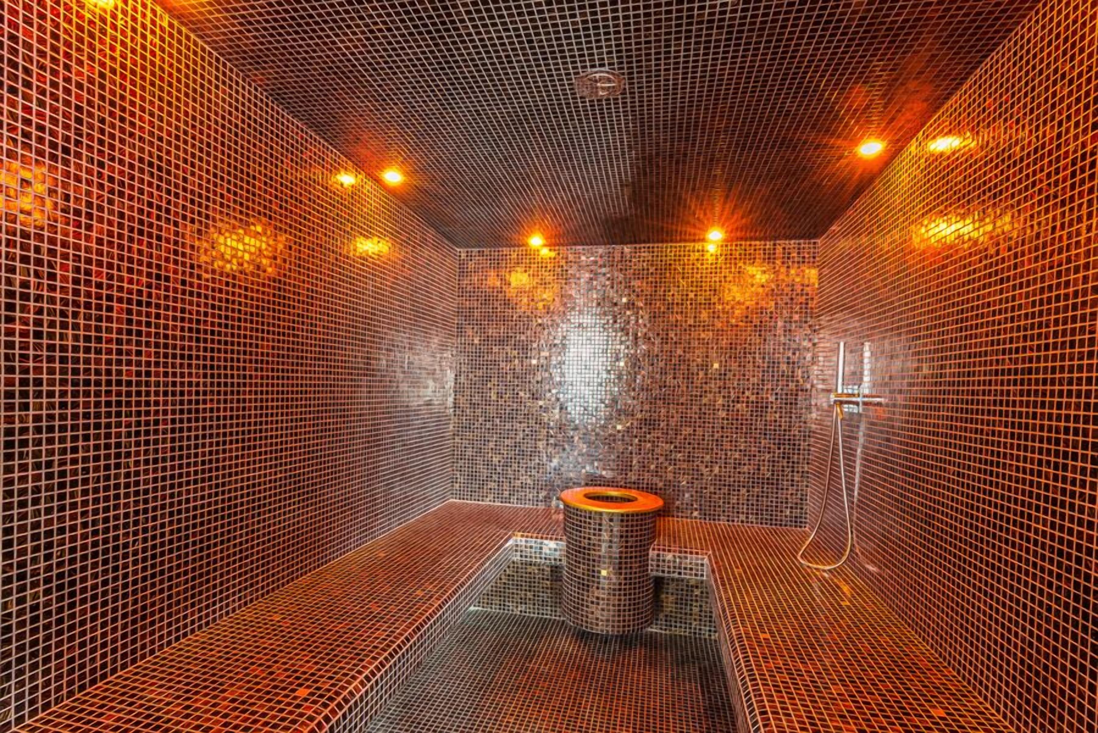 Un sauna avec un sol et des murs carrelés, un système de chauffage central et un espace douche.