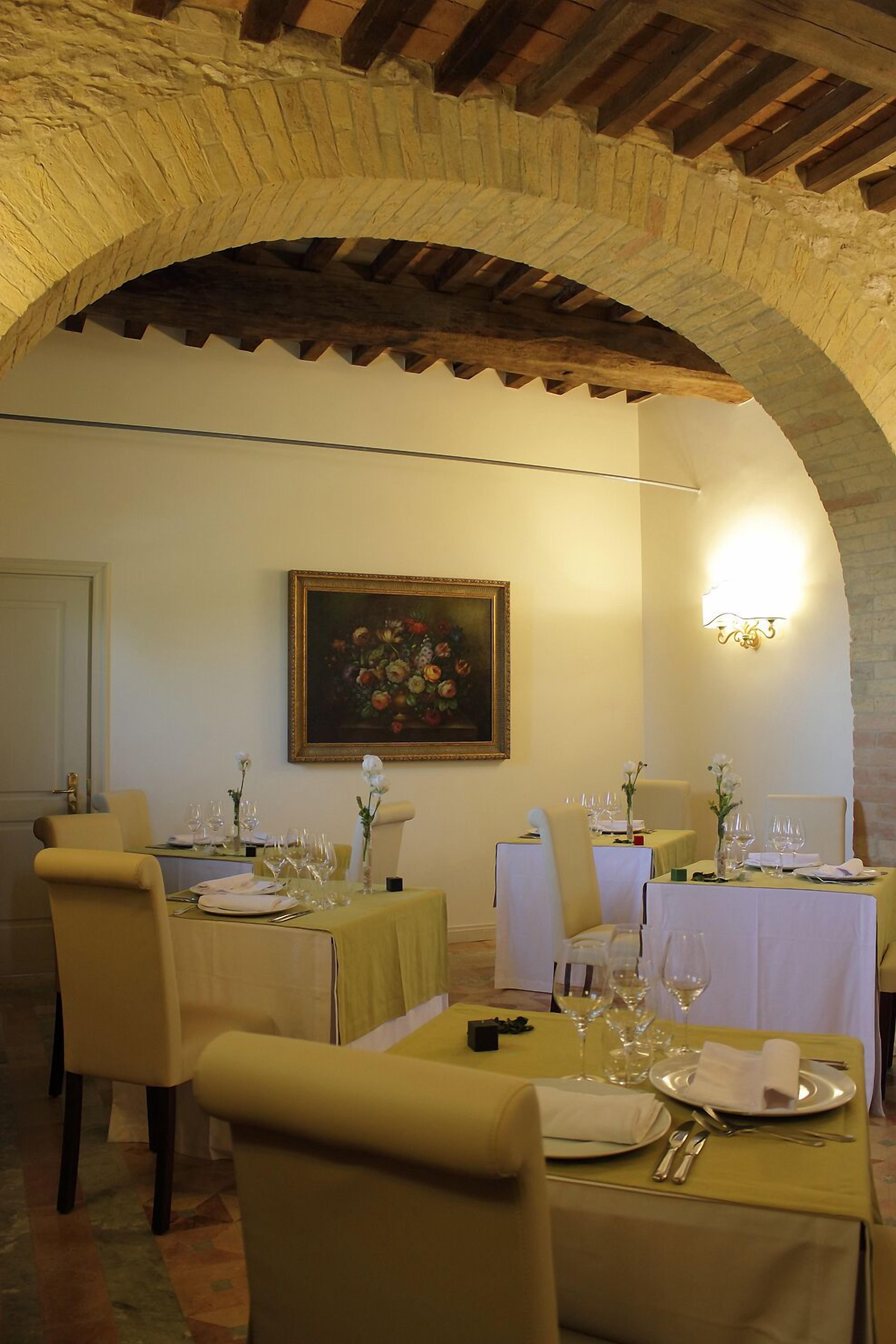 Un coin repas avec des tables préparées pour deux personnes, un tableau accroché au mur et une arche en pierre au-dessus.