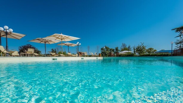A clear blue pool with lounge chairs and umbrellas. - Relais Paradiso (Gualdo Cattaneo)
