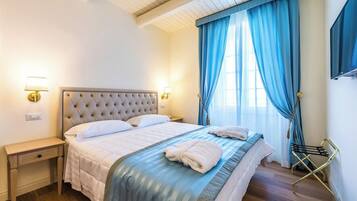 A hotel room with a tufted headboard bed, bedside lamps, a wooden nightstand, and a window with blue curtains.