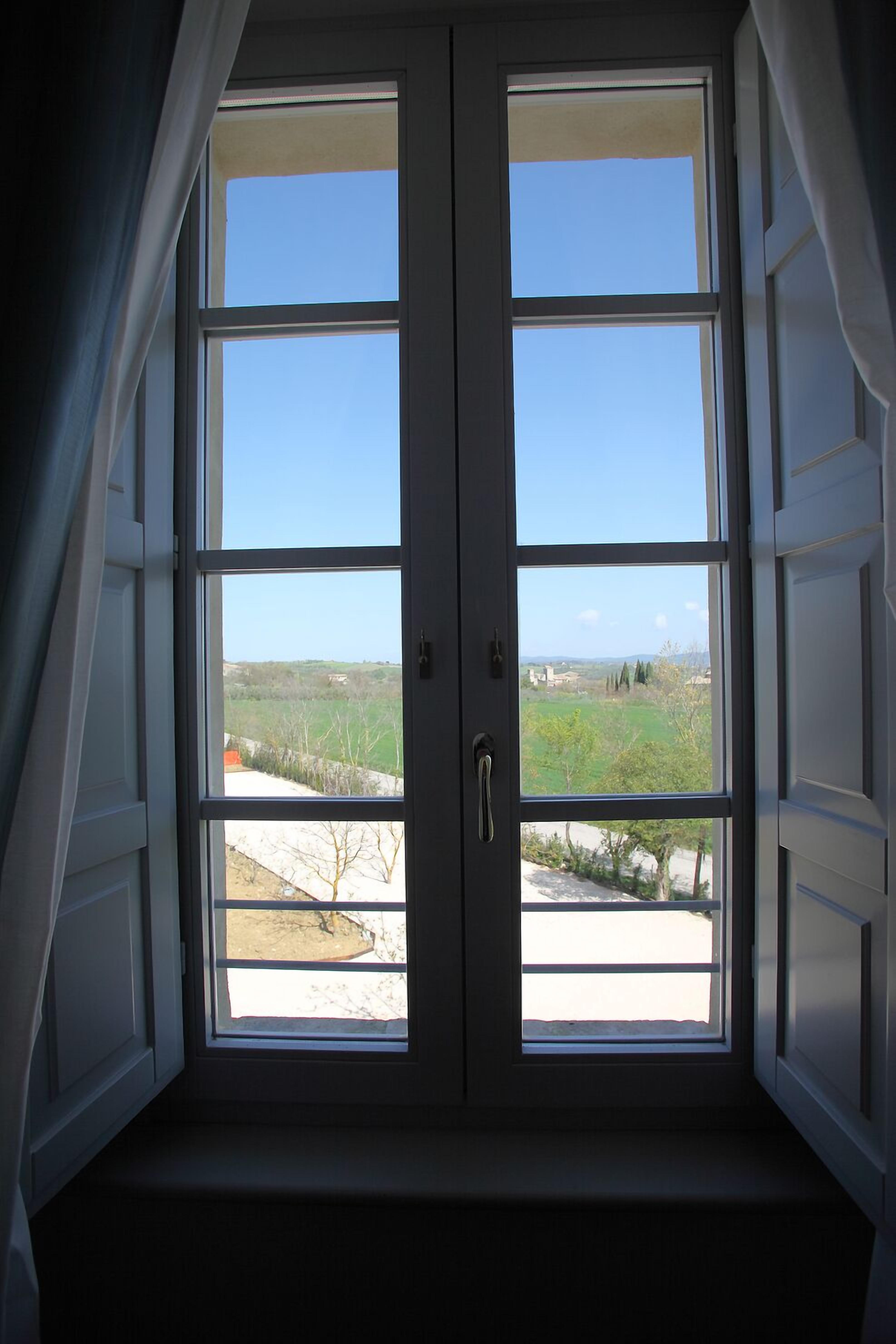 Quarto com uma janela grande que oferece vista para uma paisagem verde e edifícios ao longe.