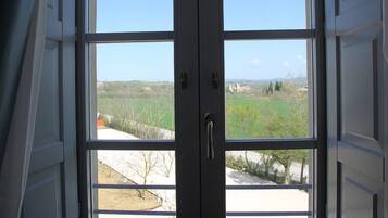 Quarto com uma janela grande que oferece vista para uma paisagem verde e edifícios ao longe.