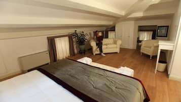 Una habitación amplia con una cama grande, una zona de estar con sofá y sillones, una planta en maceta y un televisor.