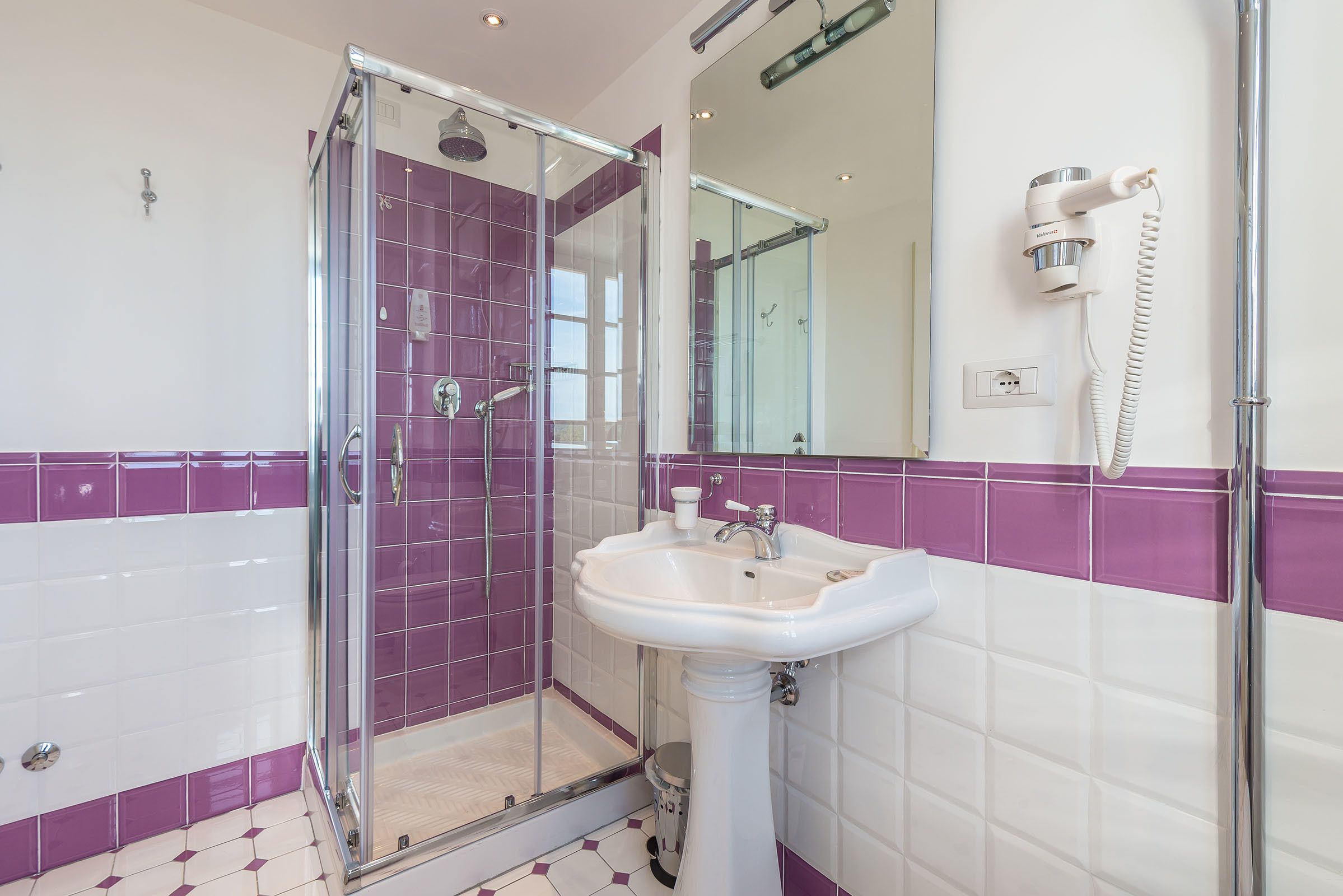 A bathroom with a glass-enclosed shower, a white sink, and purple-tiled walls.