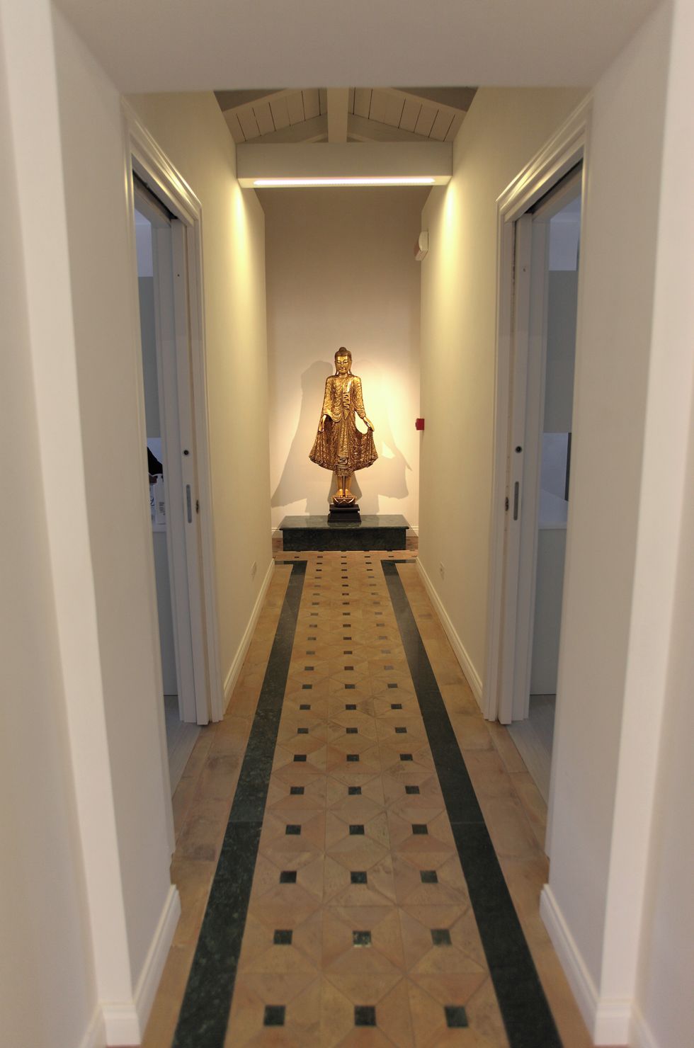 A hallway with a central statue on a pedestal, flanked by doors on either side.