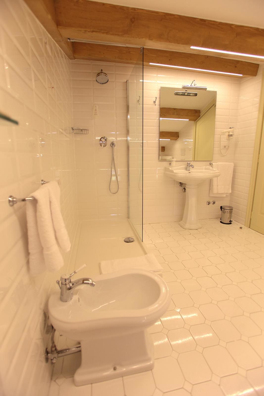 A modern bathroom with a glass-enclosed shower, a pedestal sink, and a bidet.