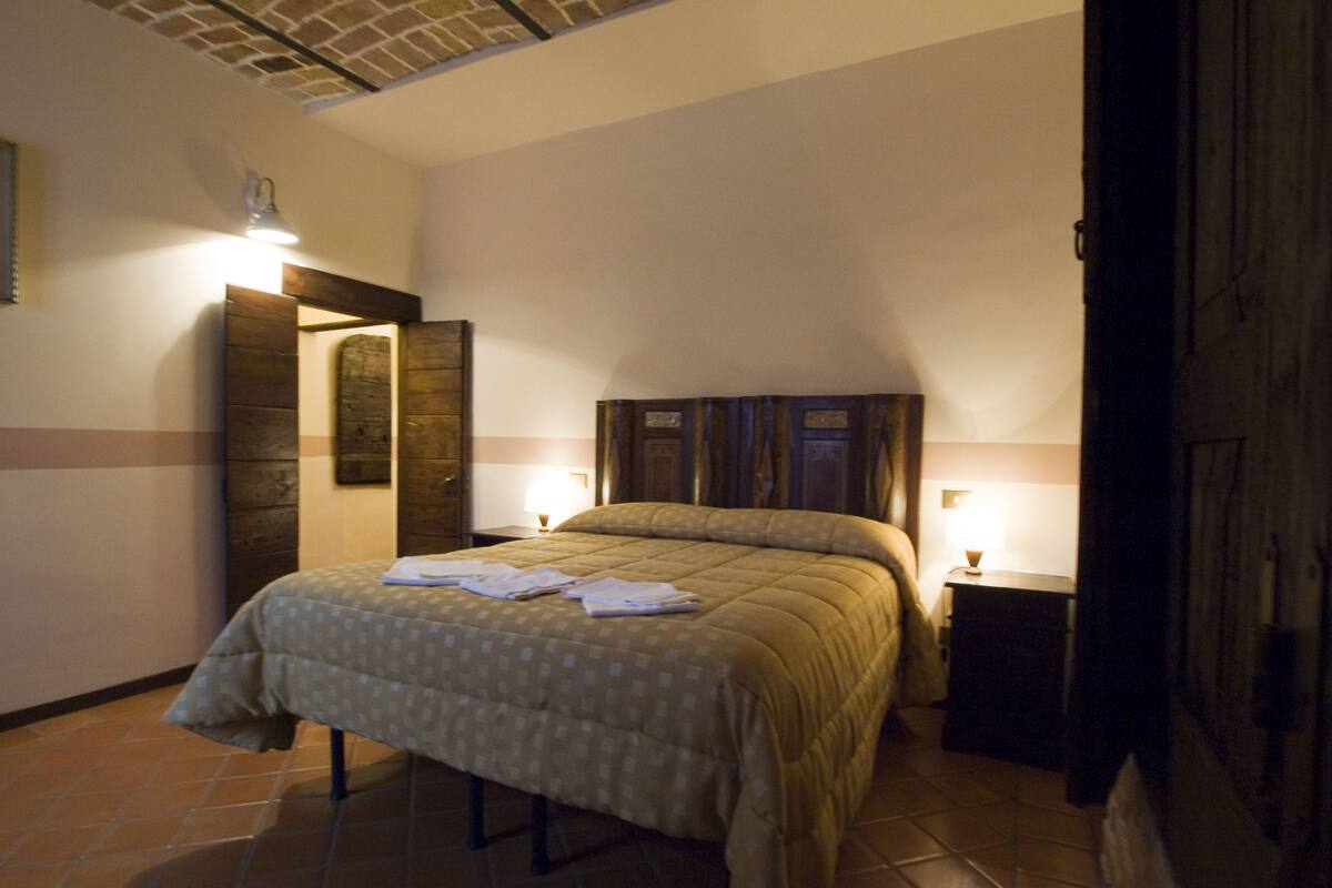 A bedroom with a bed, a nightstand, a lamp, and a wooden headboard.
