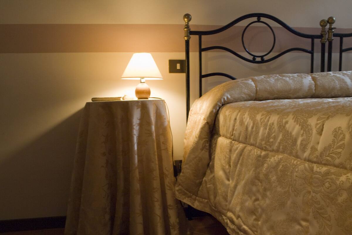 A neatly made bed with a patterned bedspread, a bedside table with a lamp, and a wall with a simple design.