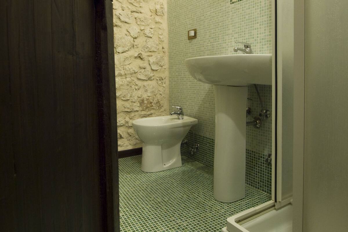 A bathroom with a stone wall, a bidet, a sink, and a shower.