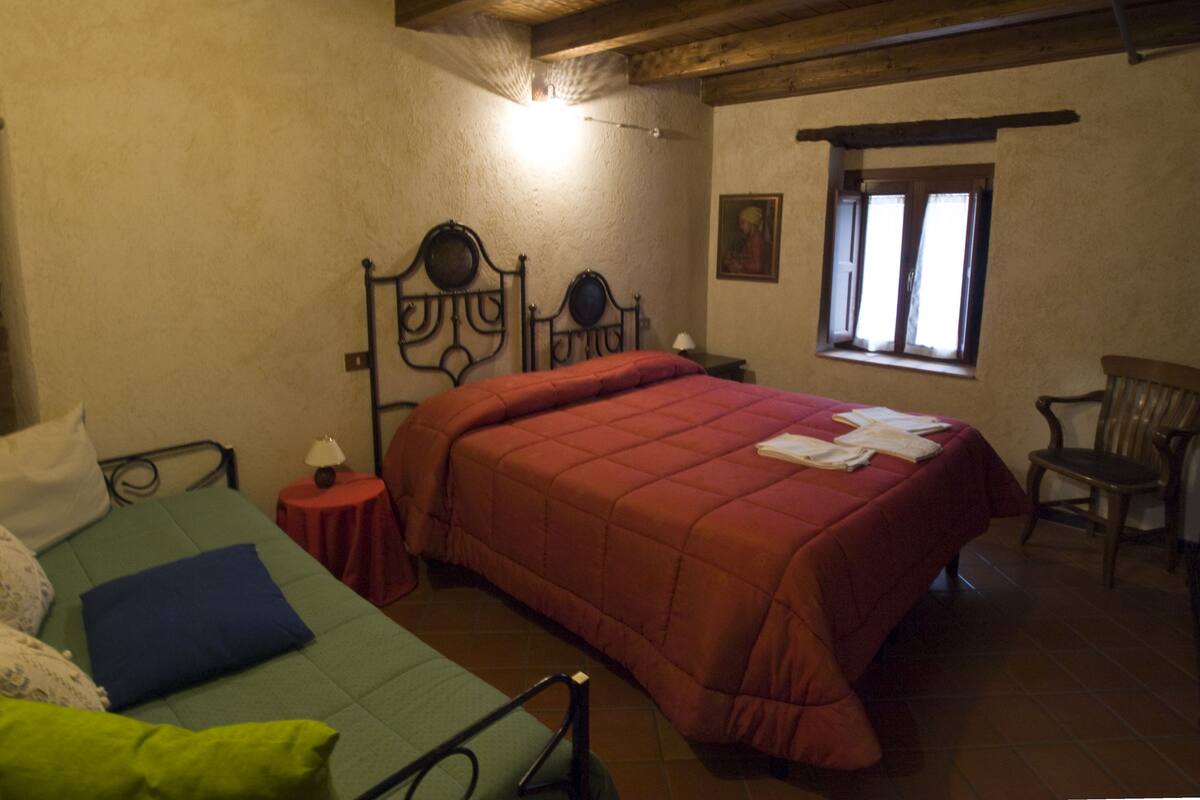 A bedroom with a bed, a chair, a small table, and a window.