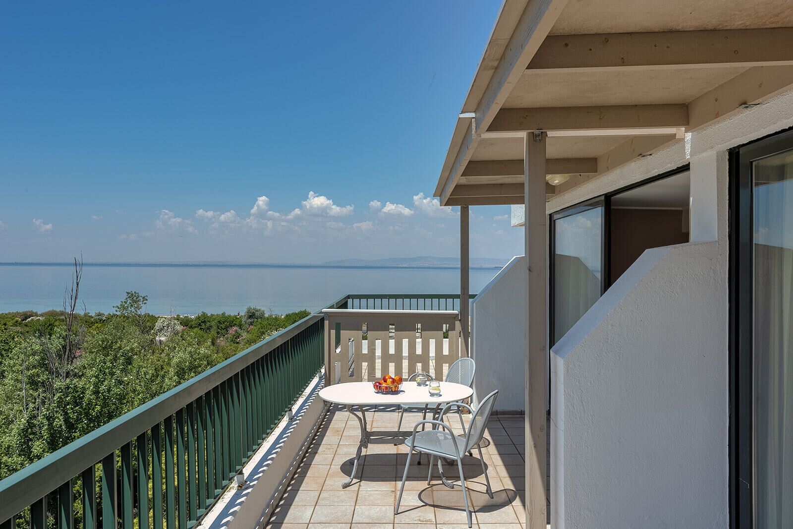 Ein Balkon mit Tisch und Stühlen, der auf ein Gewässer und Grün blickt.
