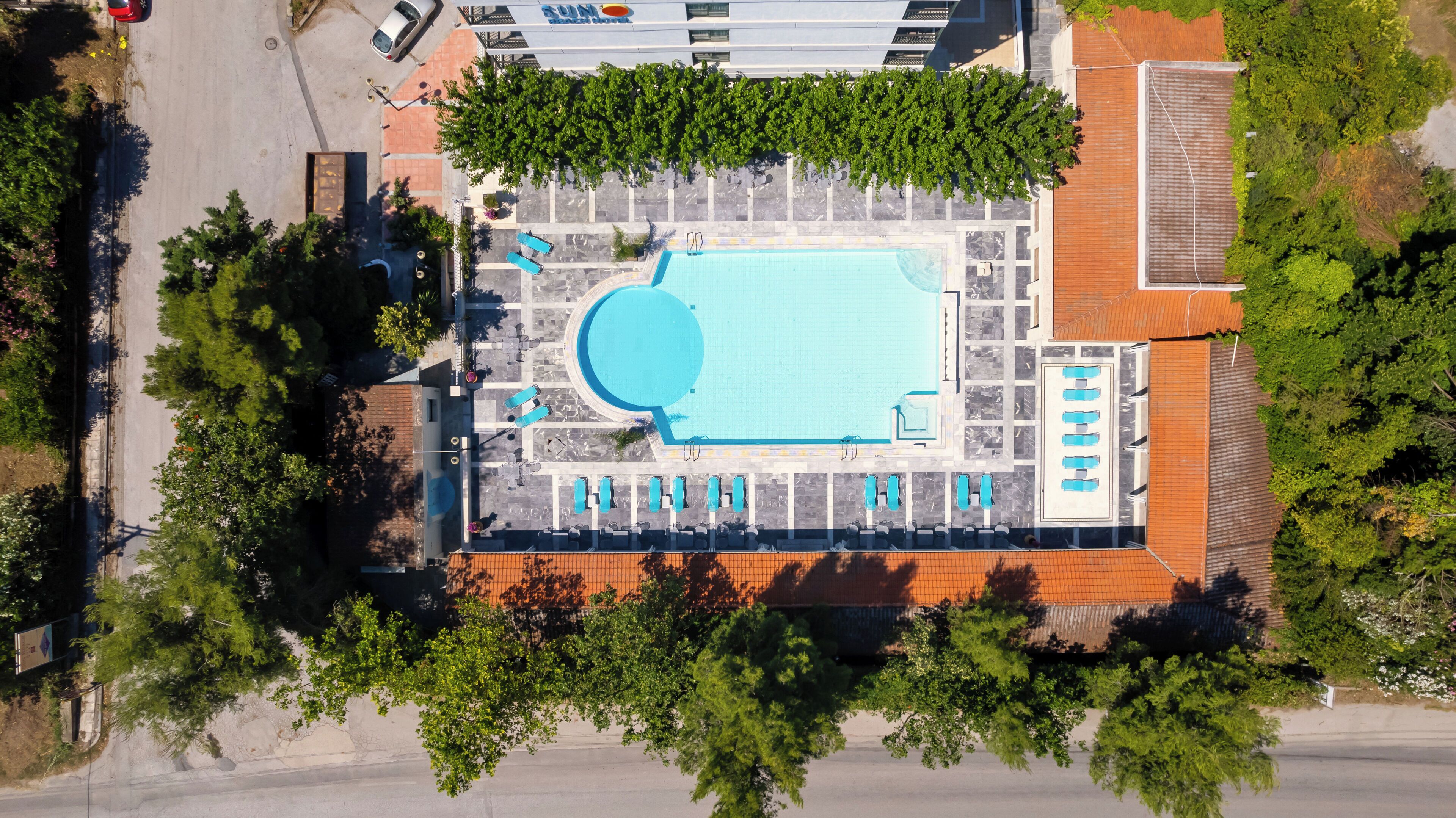 An aerial view of a hotel with a swimming pool, multiple lounge areas, and a parking lot.