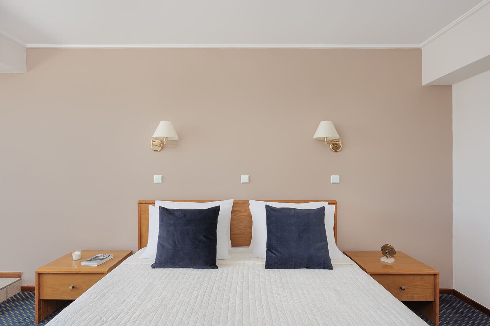 A hotel room with a large bed, two bedside tables, and two wall-mounted lamps.
