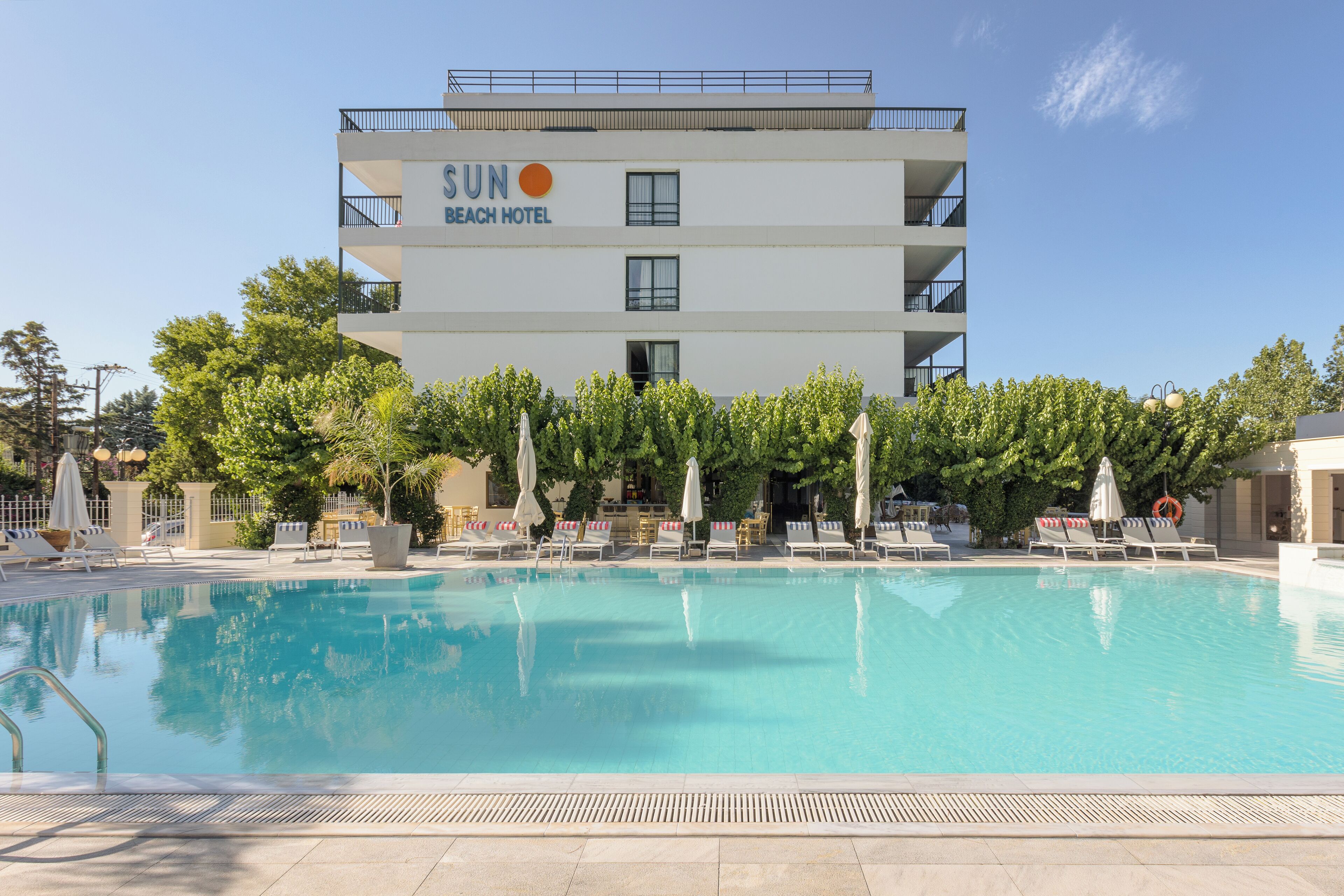 A hotel with a swimming pool, sun umbrellas, and lounge chairs.